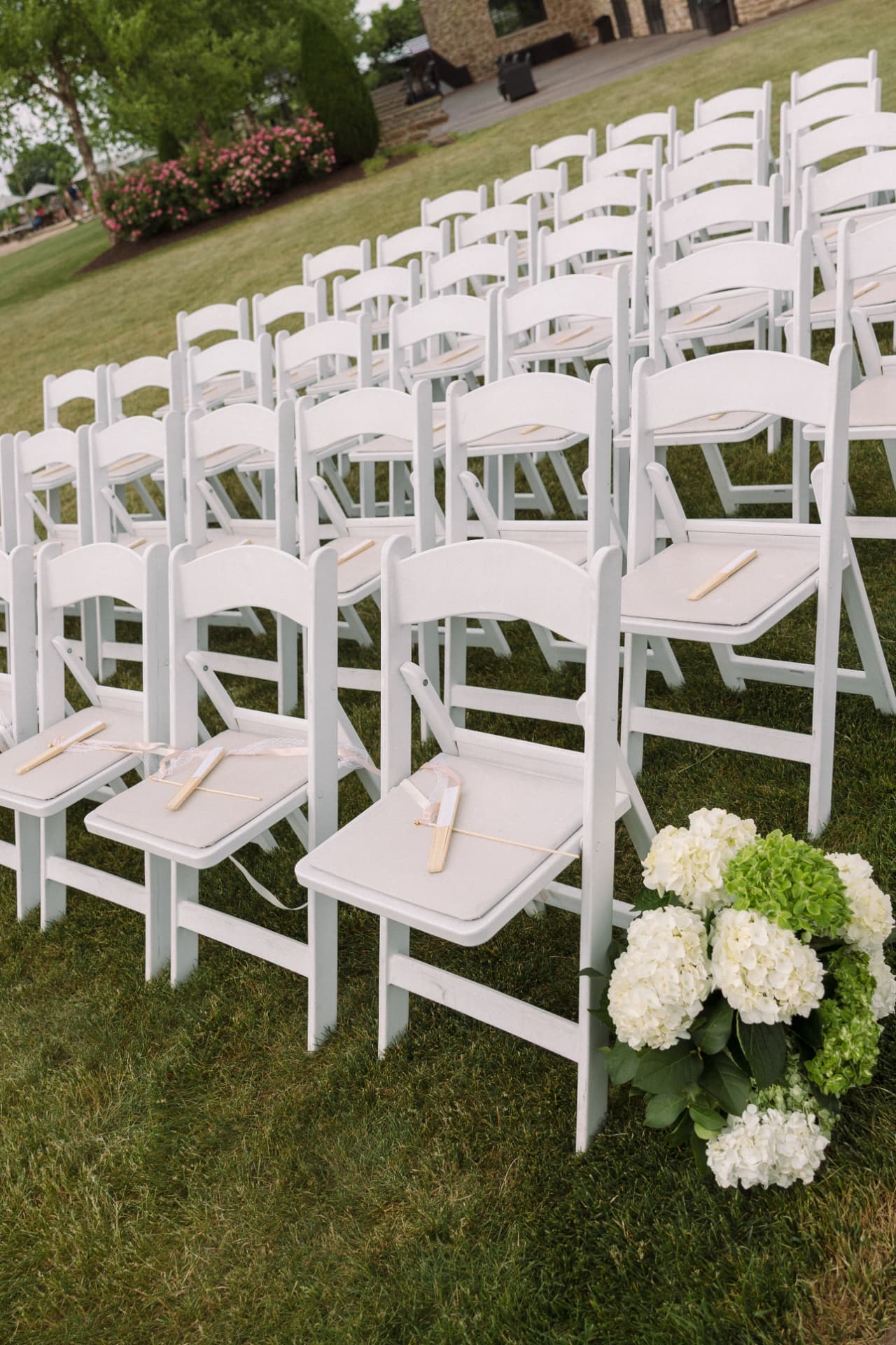 White ceremony chairs lined on the lawn with hydrangea accents